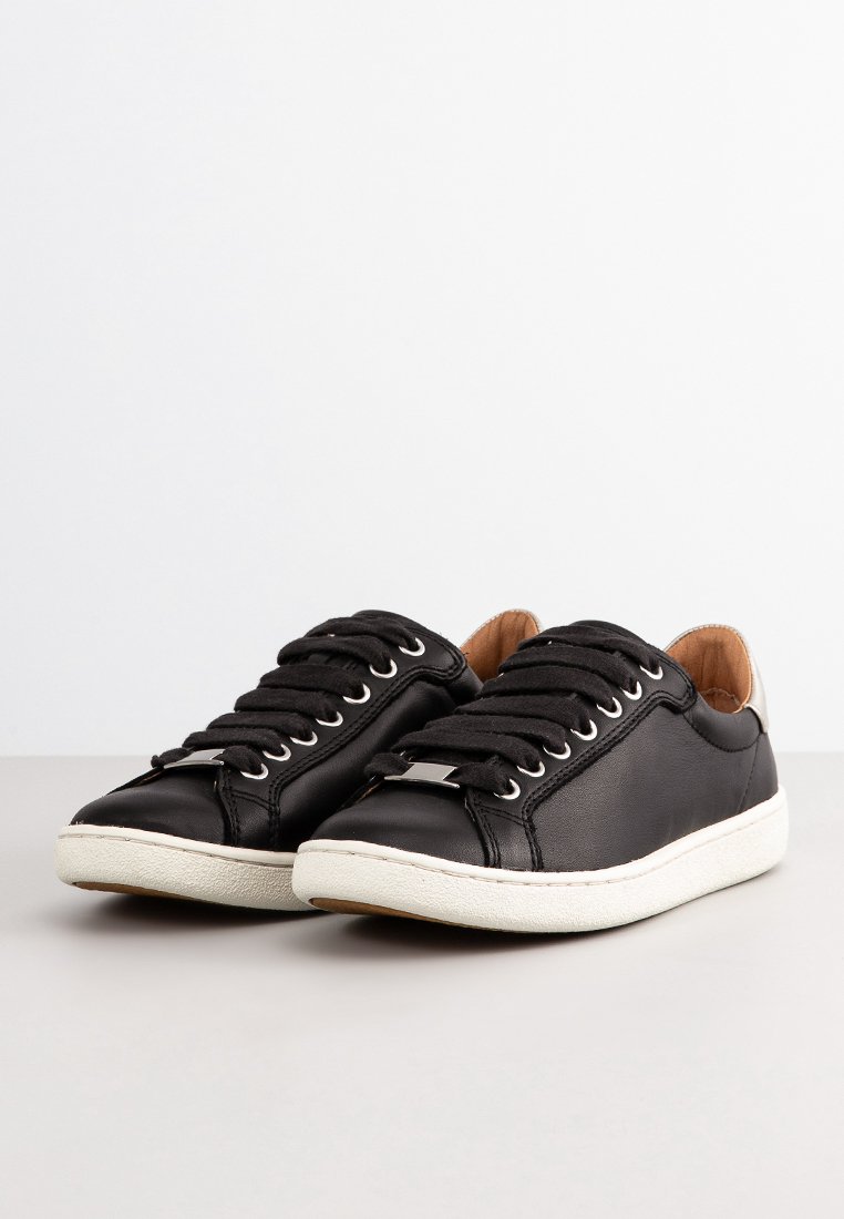 Zapatillas de cuero negro con punta redonda, suela de goma blanca, cordones negros y un sutil acento metálico en el lateral. El interior cuenta con un forro beige.