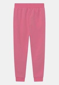 Růžové tepláky vyrobené z měkké tkaniny, s elastickým pasem a přiléhavými manžetami u kotníků. Hladký povrch bez vzorů.