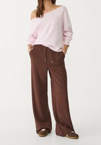 Hellrosa schulterfreies Sweatshirt mit langen Ärmeln, kombiniert mit braunen Hosen mit weitem Bein, die einen Kordelzug in der Taille und eine weiche Textur aufweisen.