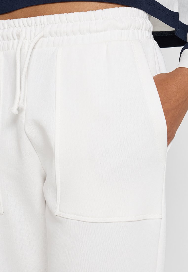 Weiße Sweatpants mit weichem Material, elastischem Bund und Kordelzug sowie tiefen Seitentaschen. Einfaches Design ohne sichtbare Muster.