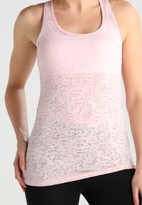 Jasnoróżowy top na ramiączkach z delikatnym fakturowanym wzorem, z wycięciem typu scoop i designem racerback. Tkanina wydaje się przewiewna i miękka.