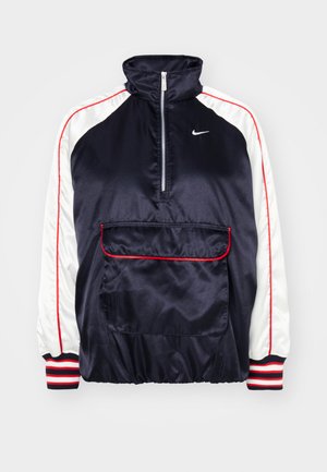 Marine satengjakke med hvite ermer, røde aksenter, halv-zip krage og en foran lomme. Har stripete ribbete mansjetter og en logo.