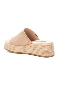 Sandalia deslizante de cuero beige con una tira ancha, suela de cuña de yute trenzado y acabado texturizado. Sutiles acentos de costura a lo largo de la tira.
