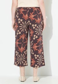 Avklippta byxor i mörk tyg, med ett djärvt mönster av röda palmträd och beige geometriska former. Elastisk midja med en avslappnad passform.