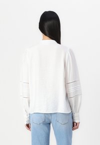 Witte textuur blouse met lange geplooide mouwen, met uitsnijdingen en een rechte zoom, gecombineerd met lichtblauwe denim broek.