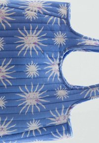 Quiltad blå handväska med ett solstrålemönster i vitt och ljust lila, med två handtag och en rundad utskärning.