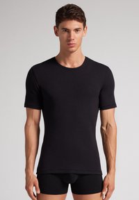 Camiseta negra de manga corta y cuello redondo, hecha de una tela suave con una textura lisa, diseño ajustado y dobladillo recto, combinada con pantalones cortos negros.