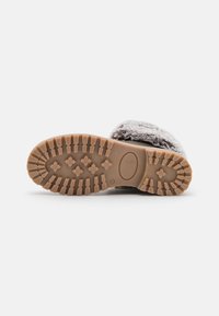 Zapatilla gris fuzzy con una textura suave y una suela de goma gruesa que presenta patrones de tracción para un buen agarre. La suela se extiende alrededor de los bordes.