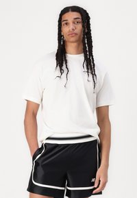 T-shirt blanc à manches courtes avec un col rond, associé à un short de sport noir avec des bordures et des rayures blanches.