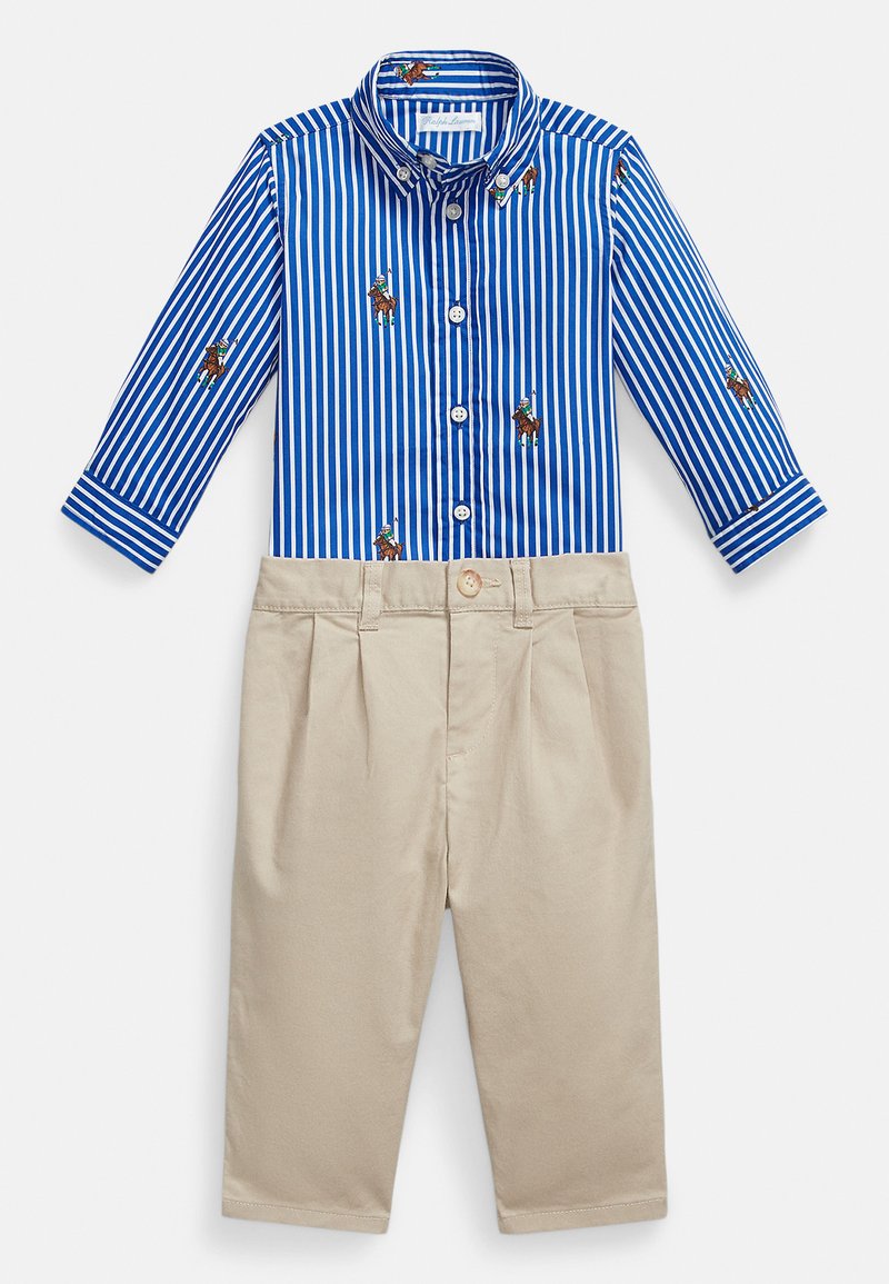 Modro-bele črtaste majica z dolgimi rokavi in vezenim motivom konja, kombinirana z bež hlačami z naborki. Opremljena z gumbi in manšetami.