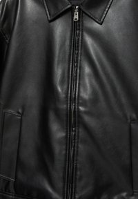 Zwarte leren jas met een opvallende kraag, ritssluiting en zijzakken, met een gladde textuur en minimale stikdetails.