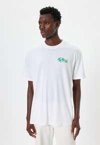 Hvid bomulds t-shirt med rund hals, korte ærmer og et grønt grafisk print, der viser en globe og ordet "UNBELIEVABLE" på forsiden.