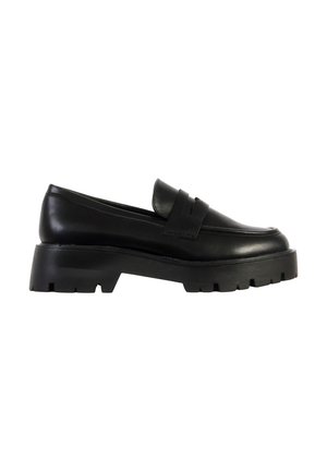 Mocassin en cuir noir à semelle épaisse, talon relevé et semelle extérieure rainurée, style slip-on avec détail de bride sur le dessus.