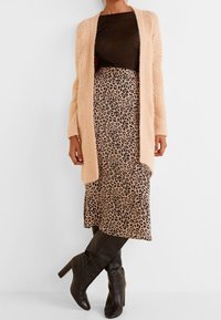 Pitkä vaaleanpunainen kardigaani, musta toppi ja leopardikuvioinen midi-hame, jotka on yhdistetty mustiin polvipitkiin korkokenkiin. Kardigaaneissa on neulottu pinta.