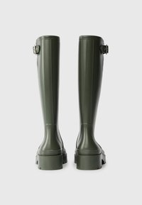 Groene rubberen kniehoge laarzen met een gestructureerde afwerking, gespaccenten en stevige, geprofileerde zolen. Stikken zijn zichtbaar langs de zijkanten.