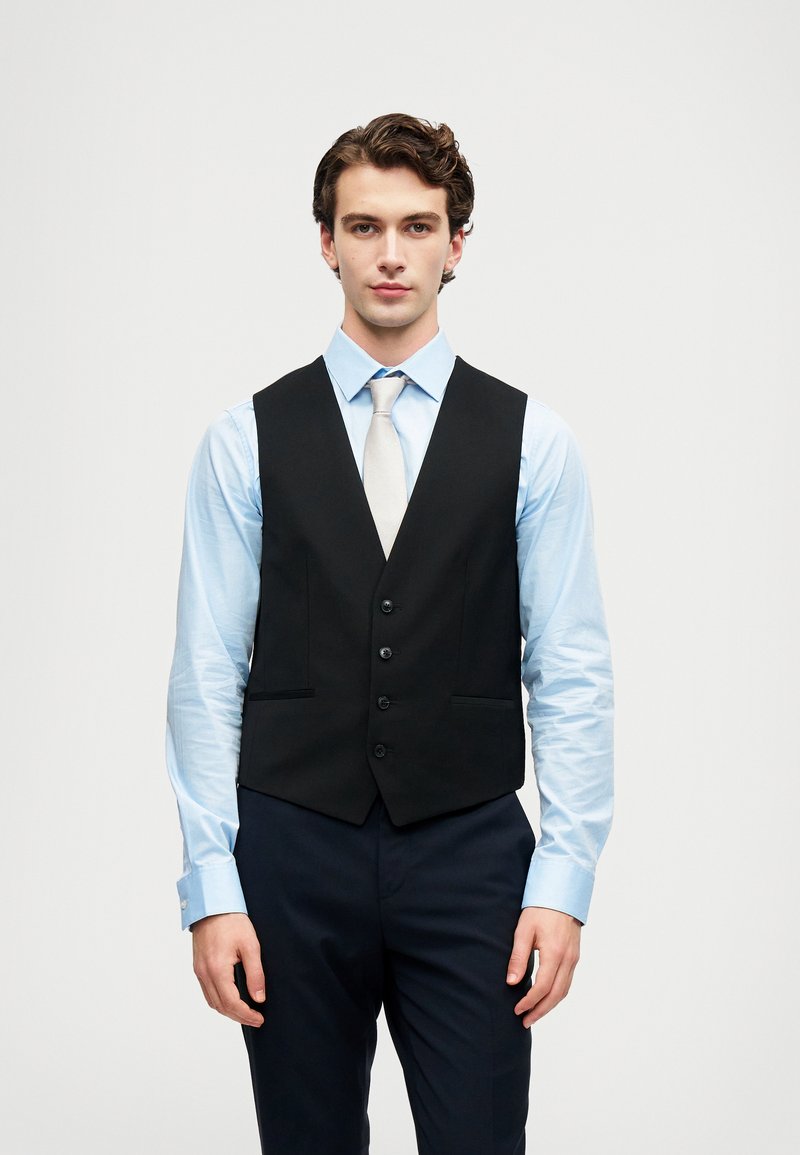 Schwarze Weste mit tailliertem Design, ausgestattet mit einer Fünf-Knopf-Verschluss und zwei Fronttaschen, getragen über einem hellblauen Hemd.