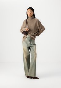 Brun strikket høyhalset genser, løs passform, kombinert med høyt liv lys blå jeans, litt falmet, og brune hæl ankelsko.