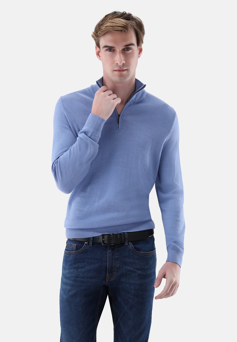 Hellblauer Reißverschluss-Pullover mit hohem Kragen, gestrickter Textur und langen Ärmeln, kombiniert mit dunklen Denim-Jeans und einem schwarzen Gürtel.