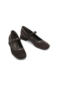 Dark brown suede flat shoes with a rounded toe, featuring a cross strap and a low block heel. The inner lining is black with gold branding.