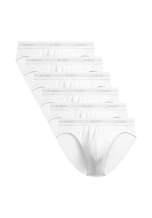 Młody muskularny mężczyzna stojący, ubrany w białe slipy z pasem "Atlantic" na jednolitym jasnym tle.