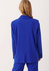 Blå skräddarsydd kavaj med spetsiga slag, slim fit, ventilerad rygg och knappade manschetter. Tillverkad av ett jämnt tyg med en klar, solid färg.