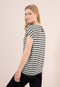 Haut à manches courtes rayé en noir et blanc, avec une coupe décontractée, un tissu texturé et un petit détail d'ouverture au dos.