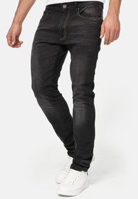 Zwarte slim-fit jeans van denim met een subtiele textuur. Heeft vijf zakken, contrasterende oranje stiksels en een knoop- en ritsluiting.