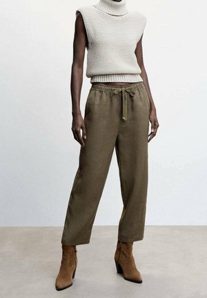 Pull à col roulé sans manches en maille crème, pantalon large taille haute olive avec cordon de serrage, et bottines à talons en daim beige sur une personne debout.