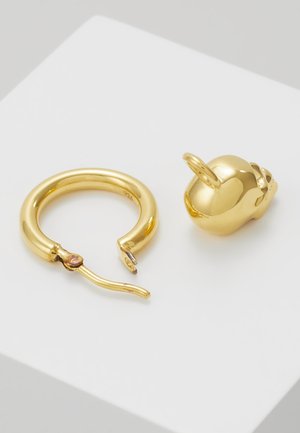 Złocone okrągłe kolczyki w kształcie koła, pokazane otwarte obok małego złotego zawieszki w kształcie czaszki z pętelką.