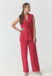 Červený padnoucí bezrukávový blazer s odpovídajícími širokými kalhotami, s hlubokým výstřihem do V a dvěma předními knoflíky, vyrobený z texturované látky.