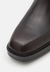 Braune Leder-Stiefelette mit strukturiertem Finish, runder Zehenpartie und schwarzer Gummisohle. Verfügt über einen Reißverschluss an der Seite.