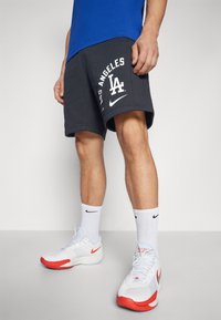 Harmaat urheilushortsit, joissa on valkoiset "Los Angeles" -teksti ja logo, yhdistettyinä valkoisiin Nike-kenkiin, joissa on punaisia yksityiskohtia, sekä valkoisiin sukkiin, joissa on musta logo.