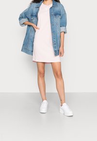 Kurtka jeansowa na jasnoróżowej, krótkiej sukience. Bielone trampki dopełniają strój. Charakterystyczne cechy to podwinięte rękawy i prosta forma.