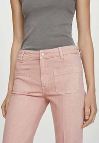 Jeans de denim rosa claro con cintura ajustada, bolsillos estándar y una ligera textura, combinados con una camiseta de tirantes gris de canalé.