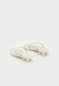 Pair of white Fenty sandals with wide straps and short block heels shaped like studs on a white background.