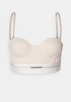 Reggiseno corto beige con ferretto e spalline regolabili. Presenta un bordo bianco con dettagli dorati e una patch con logo sul davanti.