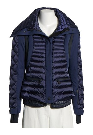 Chaqueta acolchada azul marino con bolsillos con cremallera, botones a presión y puños interiores negros, exhibida en un maniquí de torso.