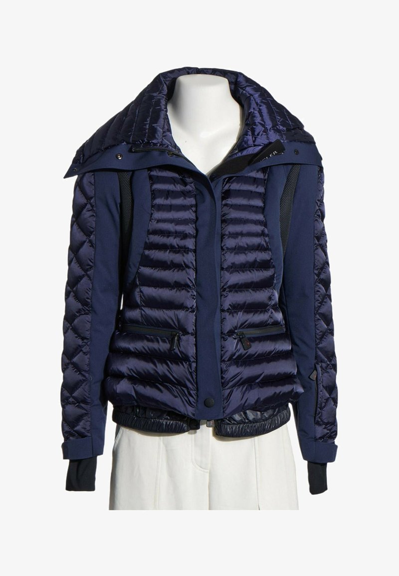 Doudoune matelassée bleu marine avec poches zippées, boutons-pression et poignets intérieurs noirs, exposée sur un mannequin buste.