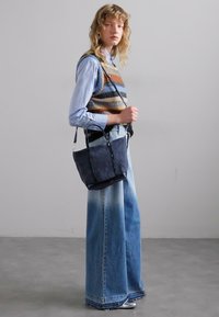 Sac en seau en denim avec une finition texturée, des bordures noires et deux poignées, associé à un jean large délavé et un gilet en maille rayé.
