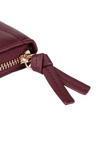 Burgundy leather wallet with gold zipper hardware, featuring a textured finish and thin leather pull tab with stitched accents.