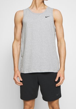 Mannelijk model dat een grijze, mouwloze Nike tanktop en zwarte Nike shorts draagt, staand met ontspannen armen langs zijn zij.