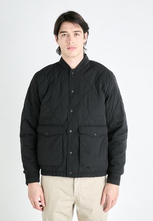 Black quilted jacket with a stand collar, snap button closure, and two front pockets. Features textured fabric and ribbed cuffs.