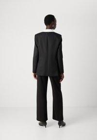 Black blazer with a contrasting white collar, tailored design, smooth fabric, paired with wide-leg black pants and ankle boots.