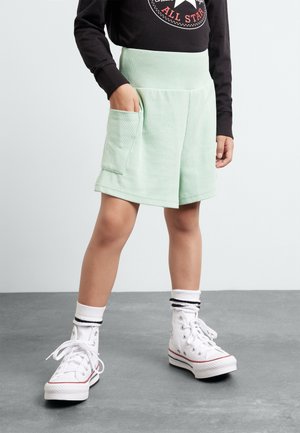 Shorts en velours côtelé vert menthe avec une large ceinture et des poches avant, associés à des baskets blanches montantes et des chaussettes à rayures.