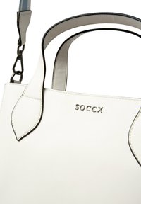 Weiße synthetische Handtasche mit gebogenen Griffen, akzentuierten Nähten und einem Metall-Logo. Verfügt über einen abnehmbaren Schulterriemen und eine strukturierte Außenseite.