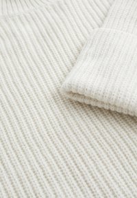 Světlý krémový pletený svetr s žebrovanou strukturou, výrazným ohrnutým rukávem a vysokým límcem. Tkanina působí měkce a silně.