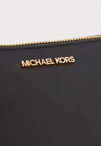 Black textured fabric pouch with a gold zipper. Features a prominent gold "MICHAEL KORS" logo on the front. Simple and elegant design.