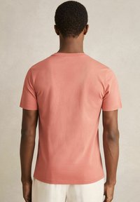 Tricou coral cu mânecă scurtă, realizat din bumbac ușor. Prezintă un gât clasic de tip crew și o suprafață netedă, fără textură.