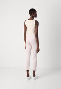 Beige tanktop, lichtroze op maat gemaakte rechte broek en witte sneakers. Eenvoudig ontwerp, gladde textuur en geen zichtbare patronen.