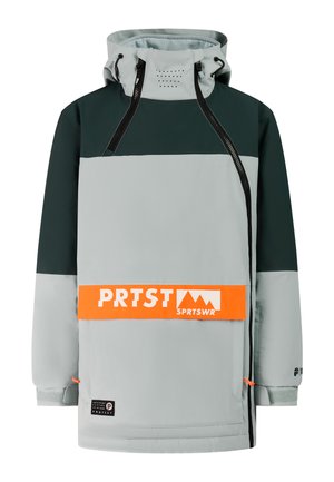 Persoon die een groene en grijze skikleding draagt met een oranje logo op de jas, een zwarte muts, regenboogreflecterende zonnebril en zwarte laarzen, rechtop staand.